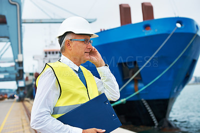 Buy stock photo A dock worker standing at the harbor amidst shipping industry activity while taking a call on his mobile