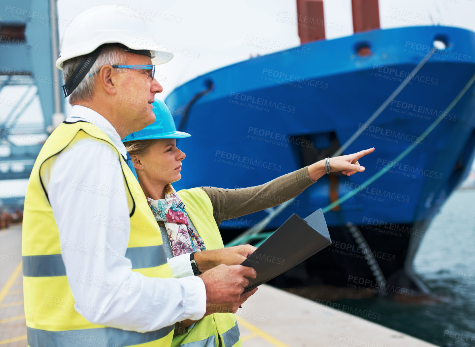 Buy stock photo Two dock workers conferring among themselves while surveying the harbor