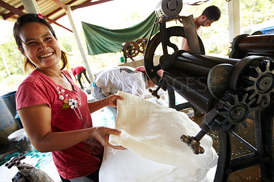 Buy stock photo A Thai woman smiles while she rolls out rubber sheets