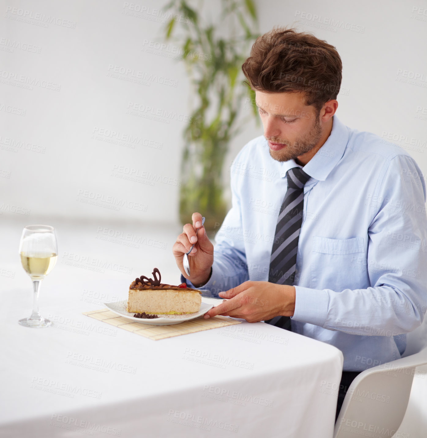 Buy stock photo Handsome young man tucking into a delicious piece of cheesecake in a restaurant