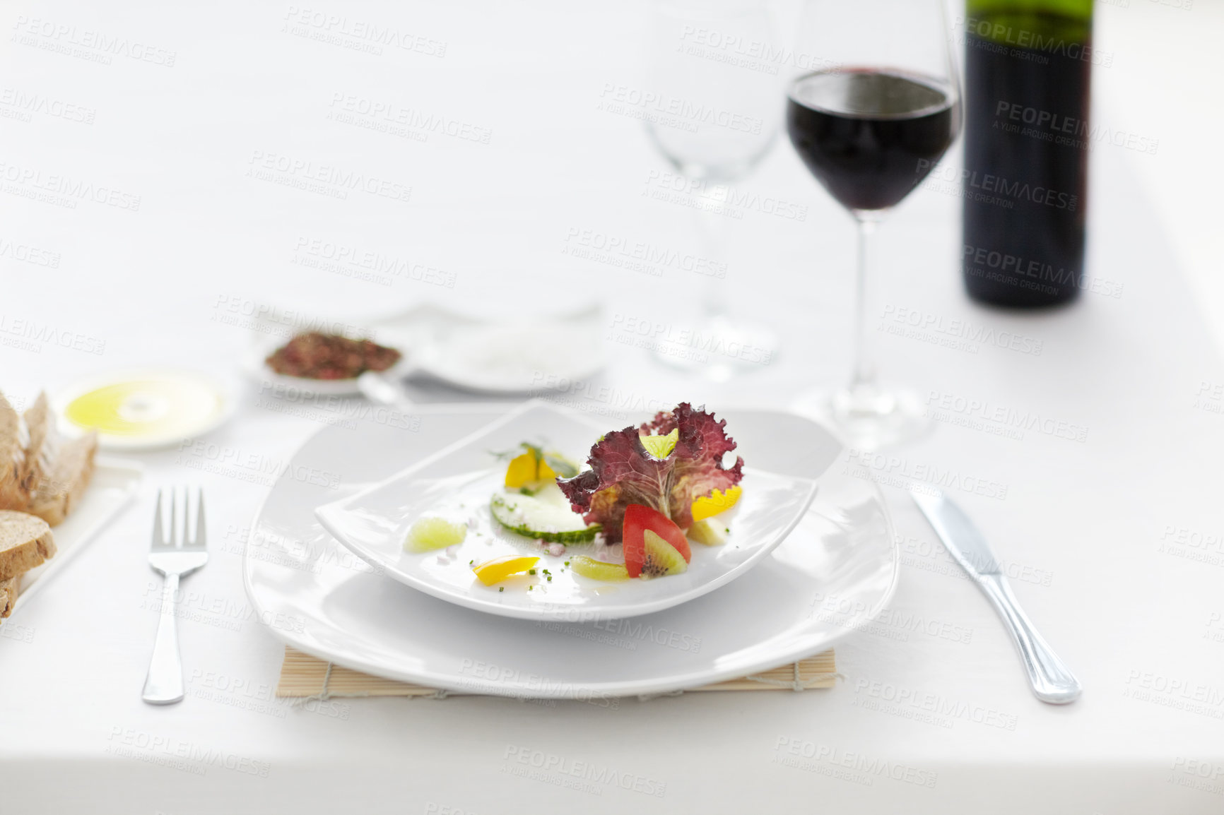 Buy stock photo A beautifully prepared salad accompanied by a glass of red wine and silver eating utensils on a white table setting in a restaurant. Healthy meal at a fancy restaurant