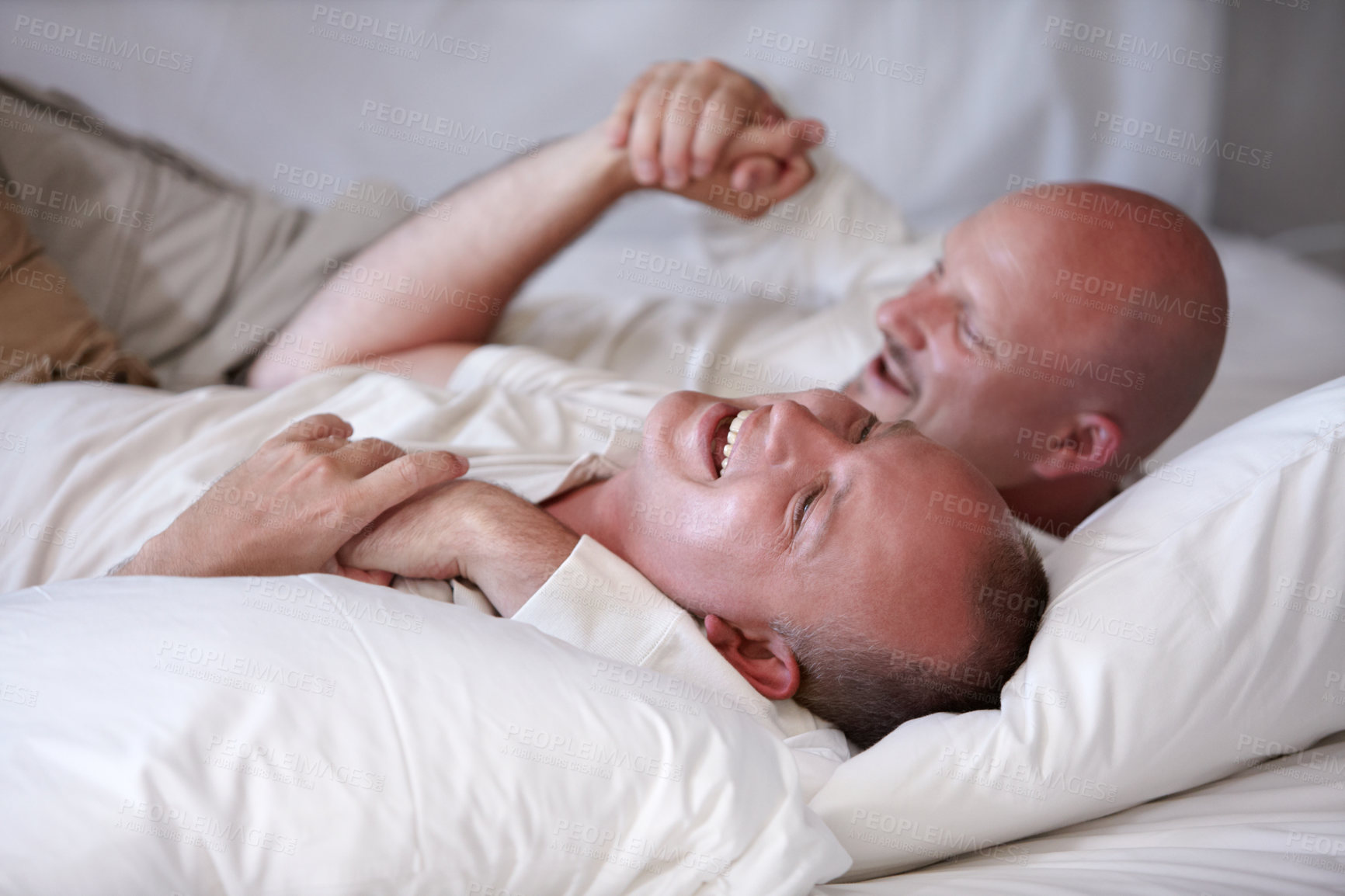 Buy stock photo Playful homosexual couple frolicking on their bed of white linen