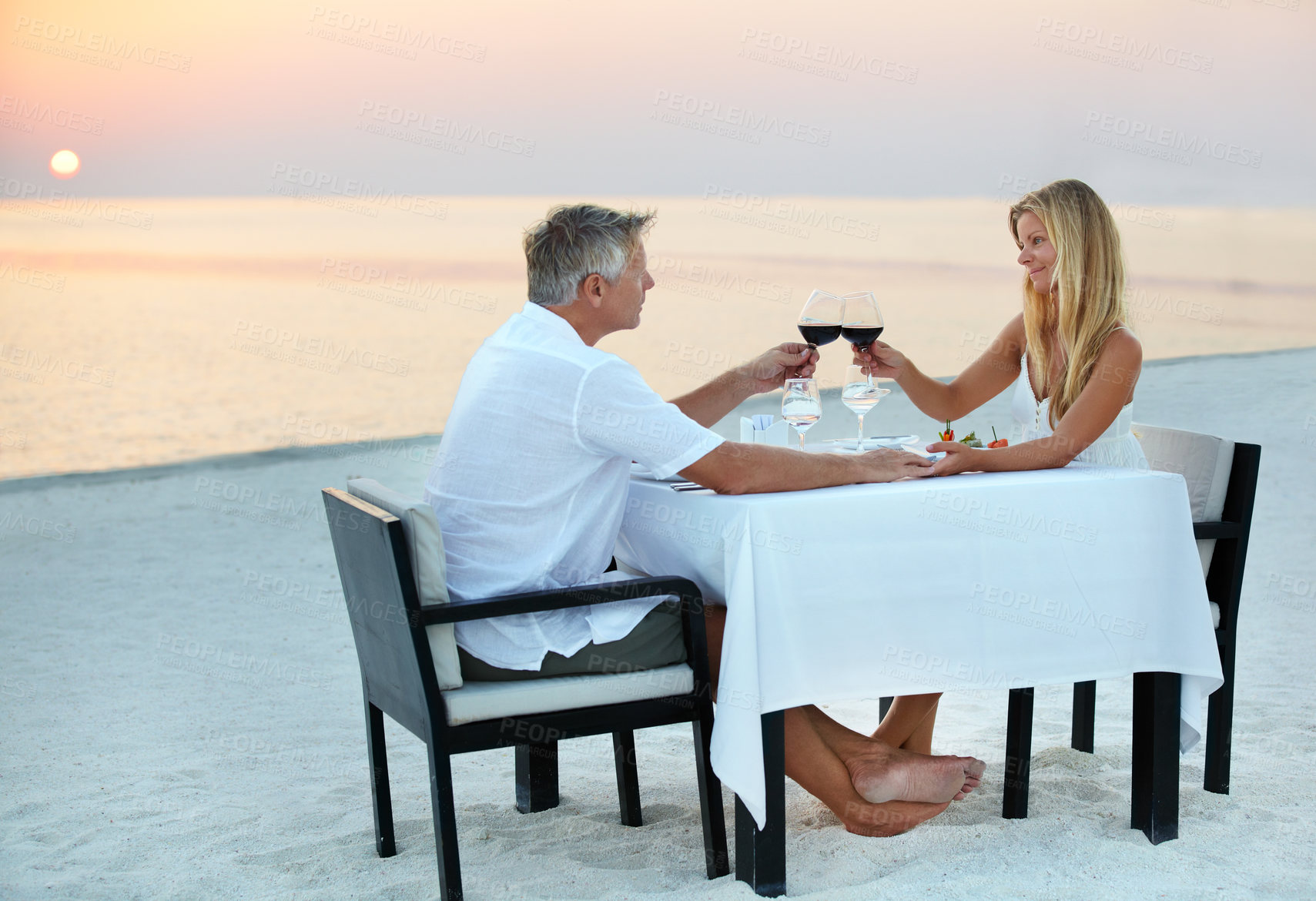 Buy stock photo Mature couple, beach and dinner in sunset for romantic outdoor date, valentines day or anniversary. Senior man and woman with wine, cheers or celebration on table in relax or romance by ocean coast