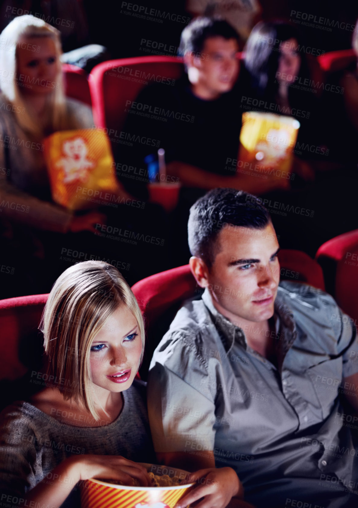 Buy stock photo Cinema, date and couple with popcorn, watching film or eating on romantic night together. Movie, man and woman in theater with snacks, show and sitting in auditorium to relax in evening with partner.