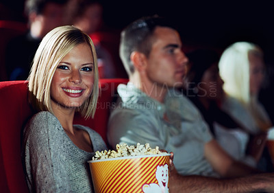 Buy stock photo A young girl eating popcorn while watching a movie at the cinema with her boyfriend
