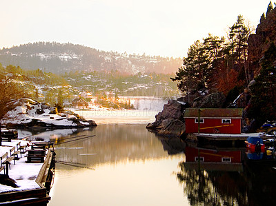 Buy stock photo Rural fishing lake in winter. Scandinavian maritime town on a sunny morning. Small village on a lake in the mountains surrounded by a snowy landscape with trees and hills. Peaceful dawn scene