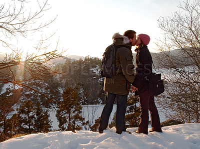 Buy stock photo Two lovers kissing as the sun sets on a snowy landscape