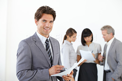 Buy stock photo A young handsome executive holding documents while his team stands in the background