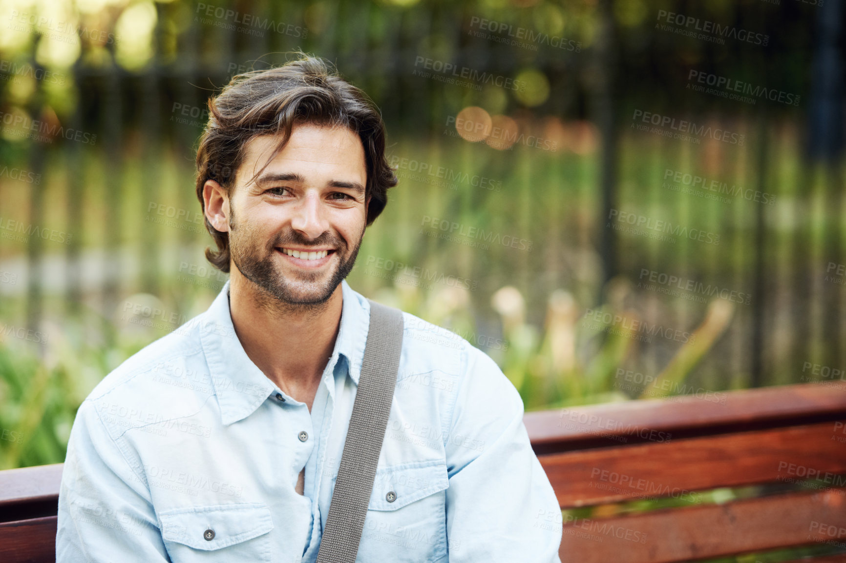 Buy stock photo Happy, relax and portrait of a man on a park bench for a break, morning commute or travel. Smile, nature and a young person or tourist in a public garden for tourism, sightseeing or a vacation