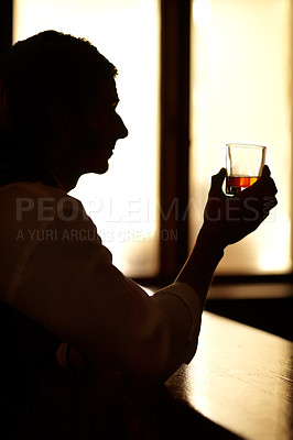 Buy stock photo Profile silhouette of a young man sitting at a bar and holding up a glass of whiskey