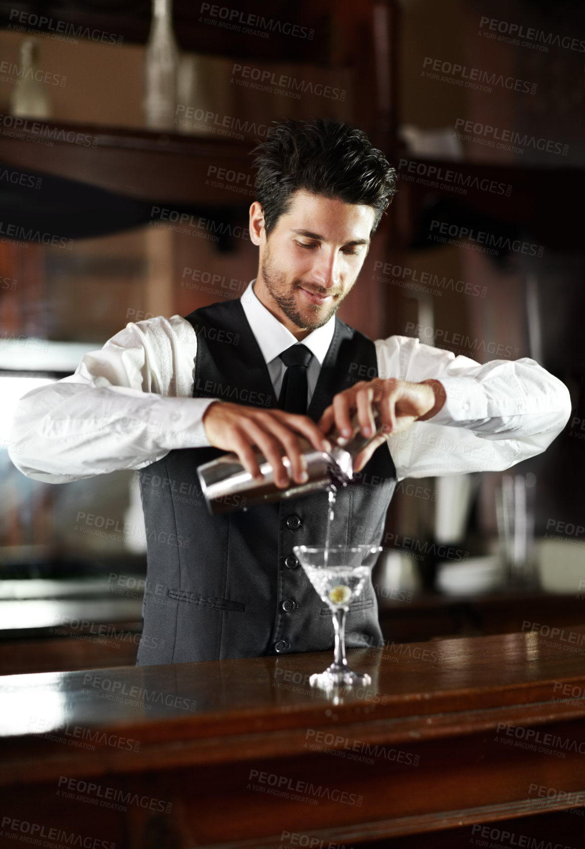 Buy stock photo A handsome young bartender mixing a cocktail for a customer