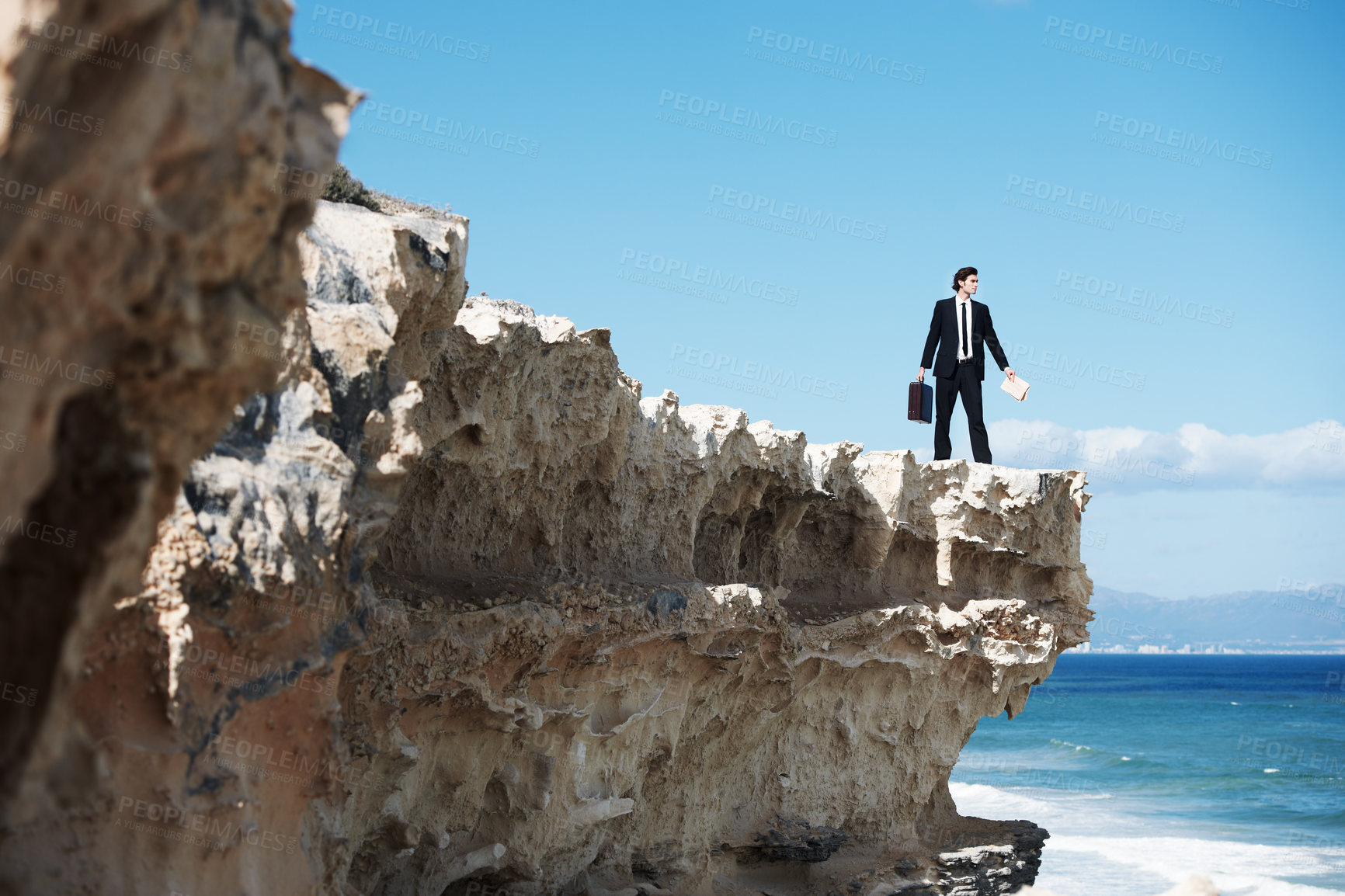 Buy stock photo Businessman standing on the edge of a cliff looking out over the ocean while holding a briefcase