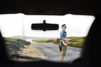 Buy stock photo Musician, travel and man with a guitar on a road trip, journey or playing instrument in countryside on highway. Guitarist, trekking and guy waiting outdoor on street for a car, van or transportation