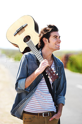 Buy stock photo Smiling young man holding his guitar over his shoulder standing on the side of the road - closeup