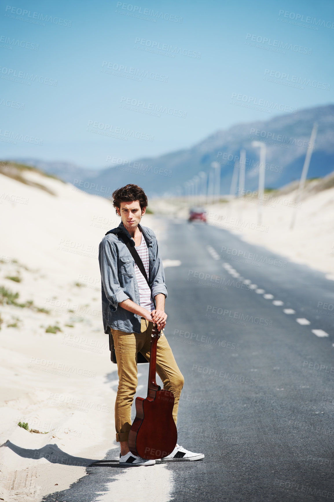 Buy stock photo Musician, travel and man with a guitar on a road trip, journey or tour in the countryside on highway. Guitarist, trekking and portrait of guy waiting on street for a car, van or transportation