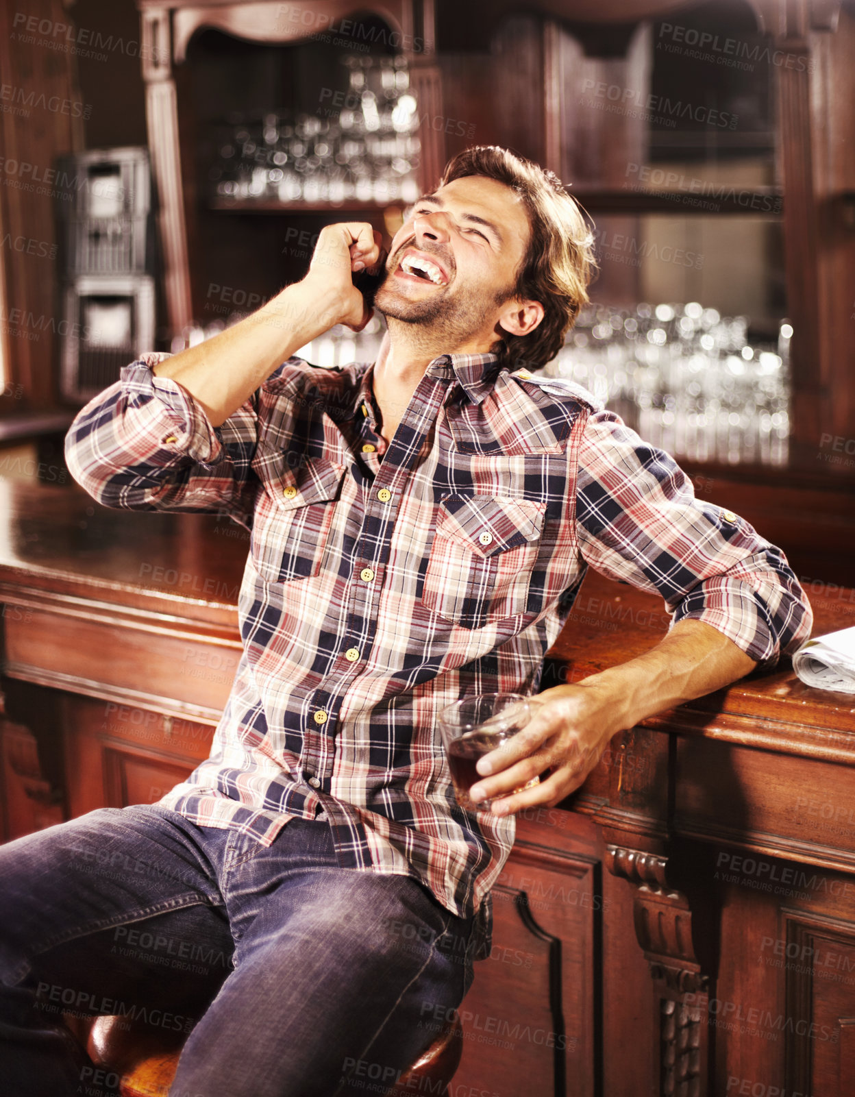 Buy stock photo Handsome young guy perched at a bar counter with a drink in hand while making a call on his mobile