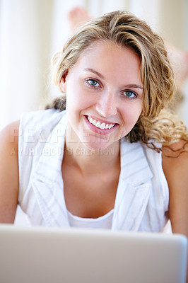Buy stock photo Portrait of a pretty young woman browsing the internet on her laptop while lying on the floor