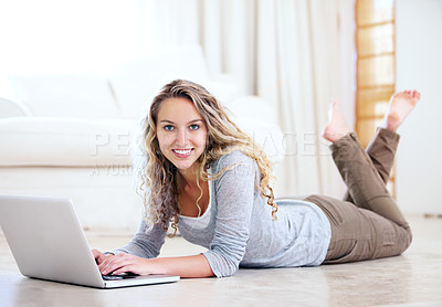 Buy stock photo Portrait of a pretty young woman browsing the internet on her laptop while lying on the floor