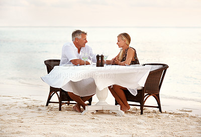 Buy stock photo Beach, dinner and couple with sunset, celebration and romance with anniversary, marriage and tropical island. People, romantic meal or man with woman, ocean and waves with summer holiday and love