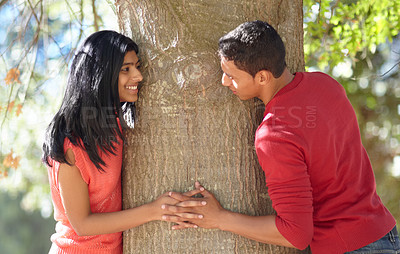 Buy stock photo Shot of a happy young couple holding hands around a tree