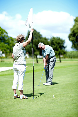 Buy stock photo A senior woman holding a flag while her husband puts for birdie