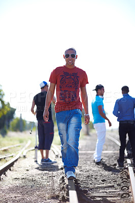 Buy stock photo Shot of a young man walking down the train tracks while his friends stand in the background