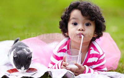 Buy stock photo Cute little girl drinking milk through a straw while lying on the grass next to her kitten