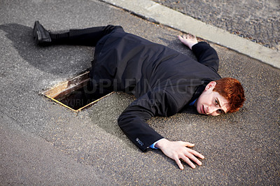 Buy stock photo A young businessman lying on the ground with his leg stuck in a drain