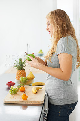 Buy stock photo Curvy and beautiful young woman cutting an apple while at her kitchen counter
