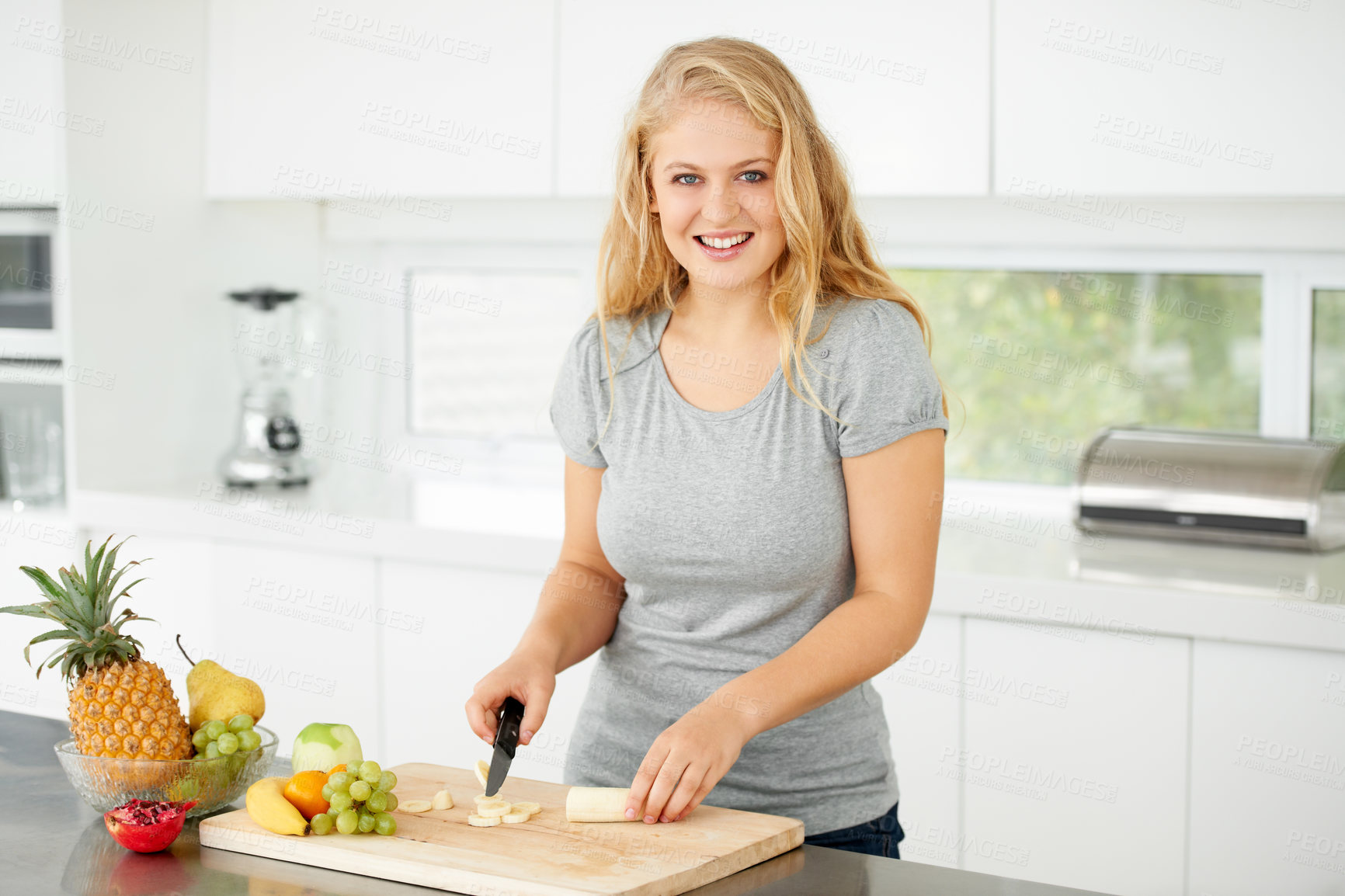 Buy stock photo Attractive curvaceous young woman chopping fruit in her kitchen