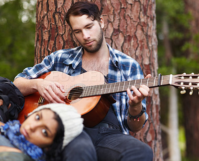 Buy stock photo Couple, playing guitar and music in forest, love and sitting together to bond, musician and sing. Relationship, relaxing and woods in nature, outdoor and guitarist for song, camping and travelling