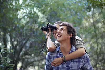 Buy stock photo A young man giving his girlfriend piggyback while she holds bincoulars