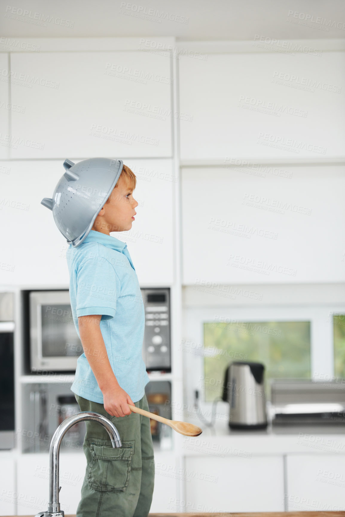 Buy stock photo A cute young boy using a rice strainer as a helmet and a wooden spoon as a sword in the kitchen