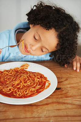 Buy stock photo Hungry, food and child eating spaghetti by the wooden kitchen counter for lunch at home. Pasta, tomato and boy kid enjoying a meal for dinner or supper for nutrition at a table in a modern house.