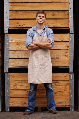 Buy stock photo Portrait of a Motivated male winemaker standing with his arms crossed in front of wooden crates of red wine in a cellar at a distillery. Young entrepreneur built his business to the point of success