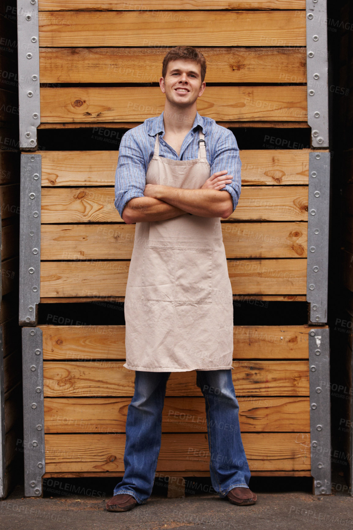 Buy stock photo Portrait of a Motivated male winemaker standing with his arms crossed in front of wooden crates of red wine in a cellar at a distillery. Young entrepreneur built his business to the point of success