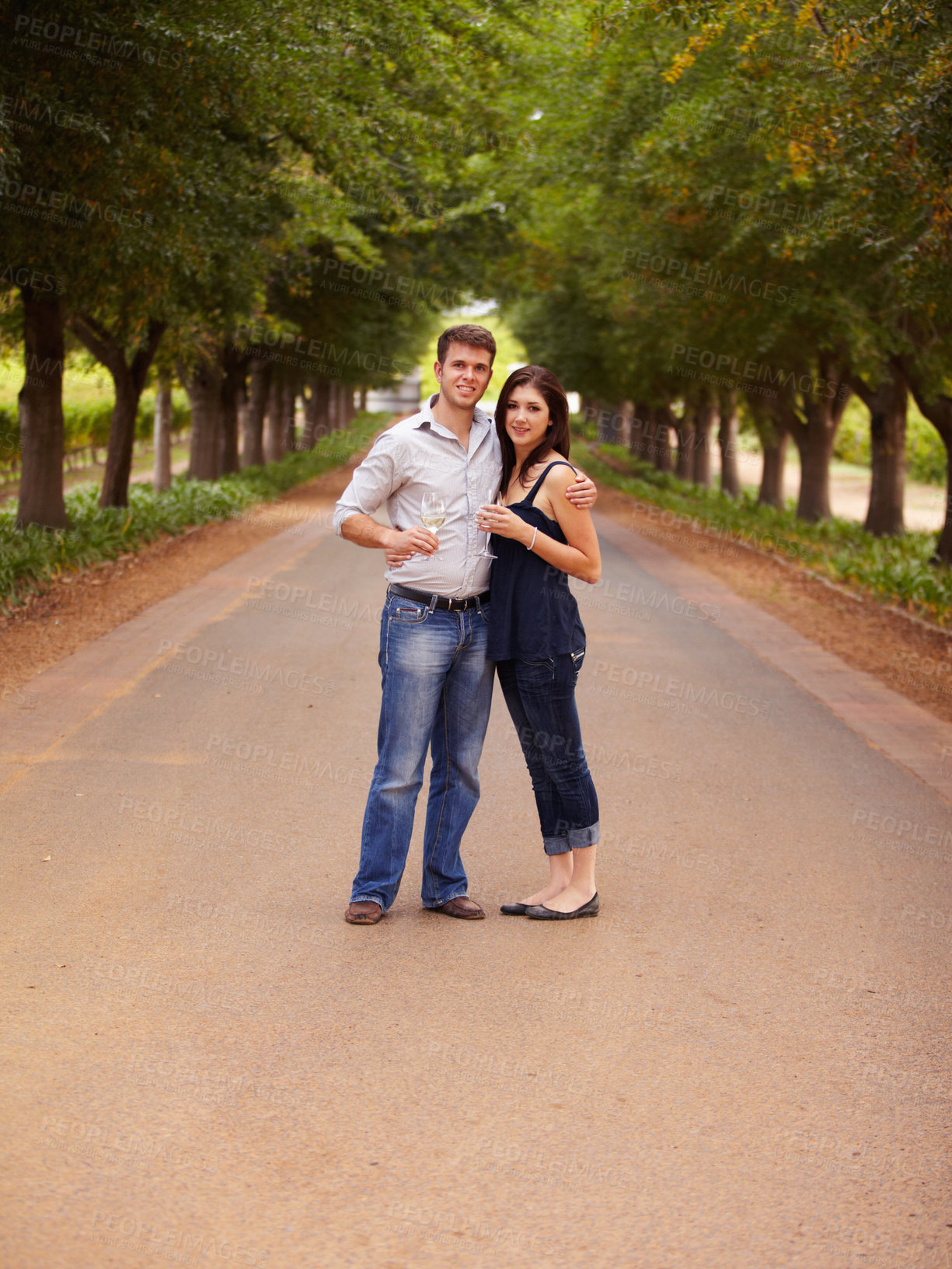 Buy stock photo Couple, portrait and wine outdoor at a vineyard for vacation, holiday or travel with love and care. Man and a woman hug on a countryside road with trees, alcohol glass or drinks to celebrate marriage