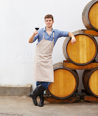 Buy stock photo Portrait, wine and oak barrels with a man holding a glass in a winery or distillery as an artisan and sommelier. Drink, red blend and alcohol with a male beverage maker in a factory or warehouse