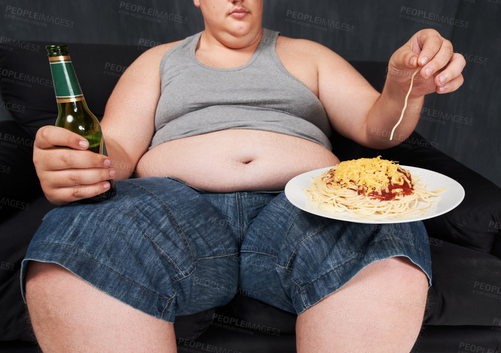 Buy stock photo A cropped shot of an obese young man sitting on a sofa and eating spaghetti with his hands