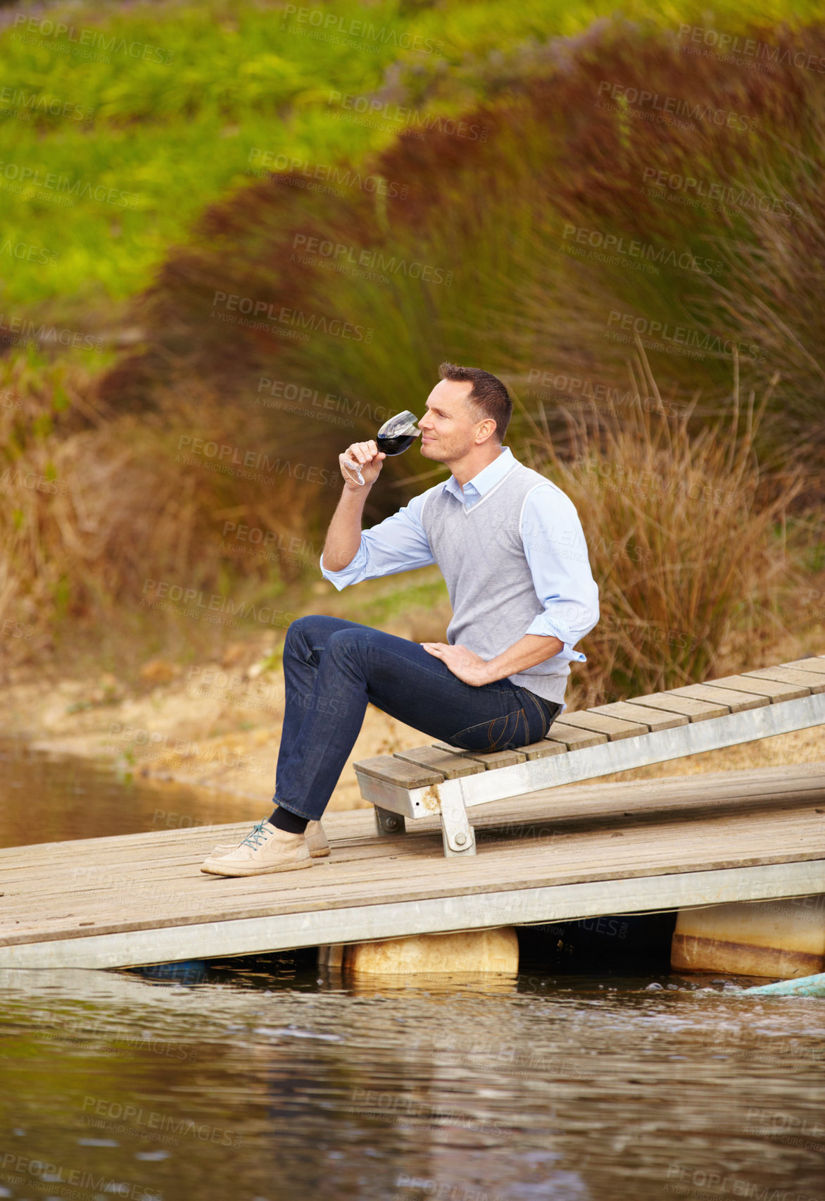 Buy stock photo Thinking, river and a man drinking wine outdoor in nature on his farm for agriculture or sustainability. Water, glass and idea with a male person sitting on the pier to drink alcohol alone outside