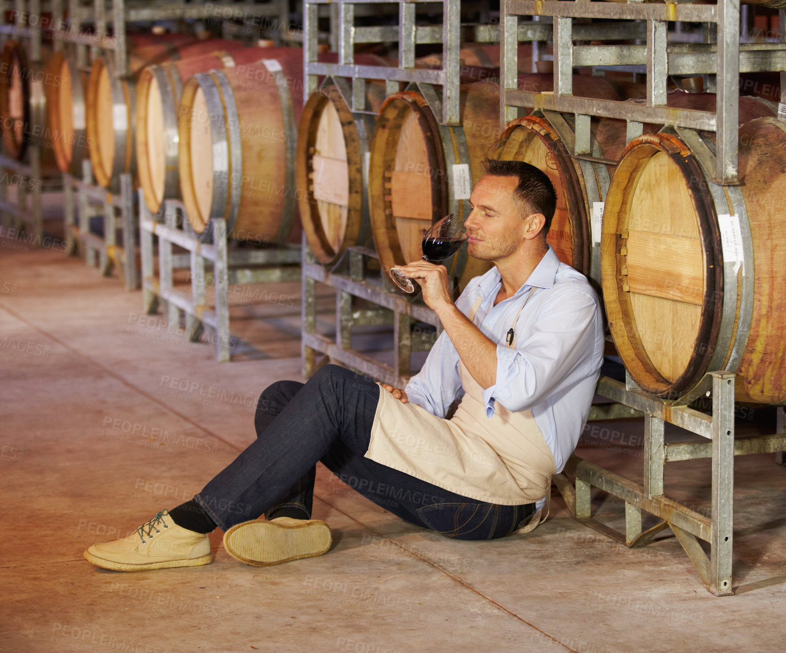 Buy stock photo Cellar, mature man wine tasting and sitting by a barrel in a warehouse. Wood cask storage, aging drink and a male sommelier holding or drinking a glass of alcohol or red blend in a factory working