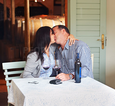 Buy stock photo Love, kiss and a couple on a wine farm together in celebration of love or their anniversary. Kissing, romance or dating with a loving man and woman at a table in a winery feeling happy while bonding