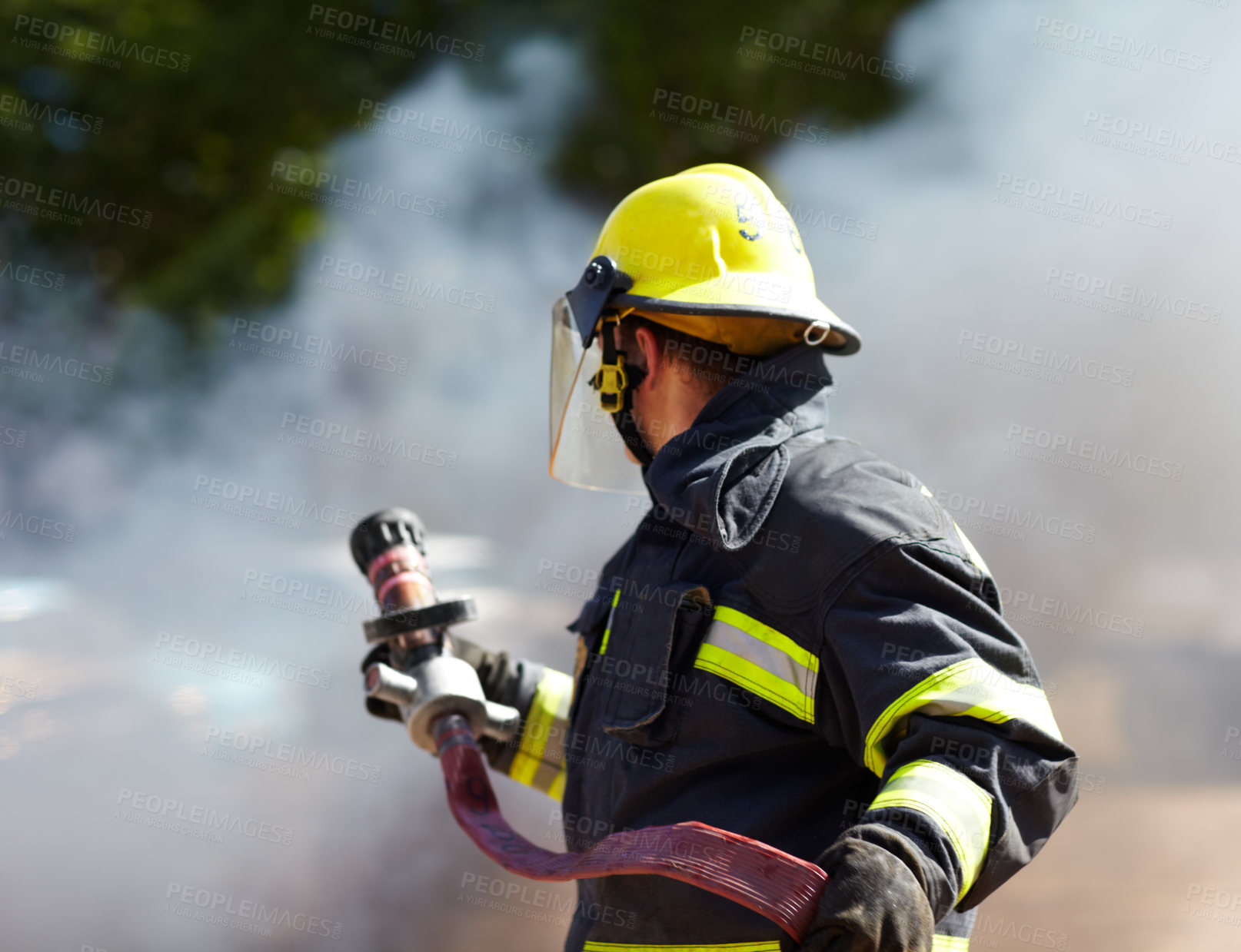 Buy stock photo A caucasian fireman holding a hose and surrounded by the smoke from the fire he's just extinguished