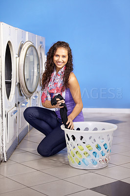 Buy stock photo Portrait of a young attractive woman kneeling as she places her clothes in the washing machine at the laundry