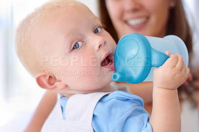 Buy stock photo Portrait, family and a baby boy drinking water from a bottle with his mother in the blurred background. Face, kids and hydration with a young child in his home for a drink during child development