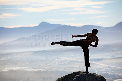 Buy stock photo A male kickboxer practising his kicking technique on a mountain peak