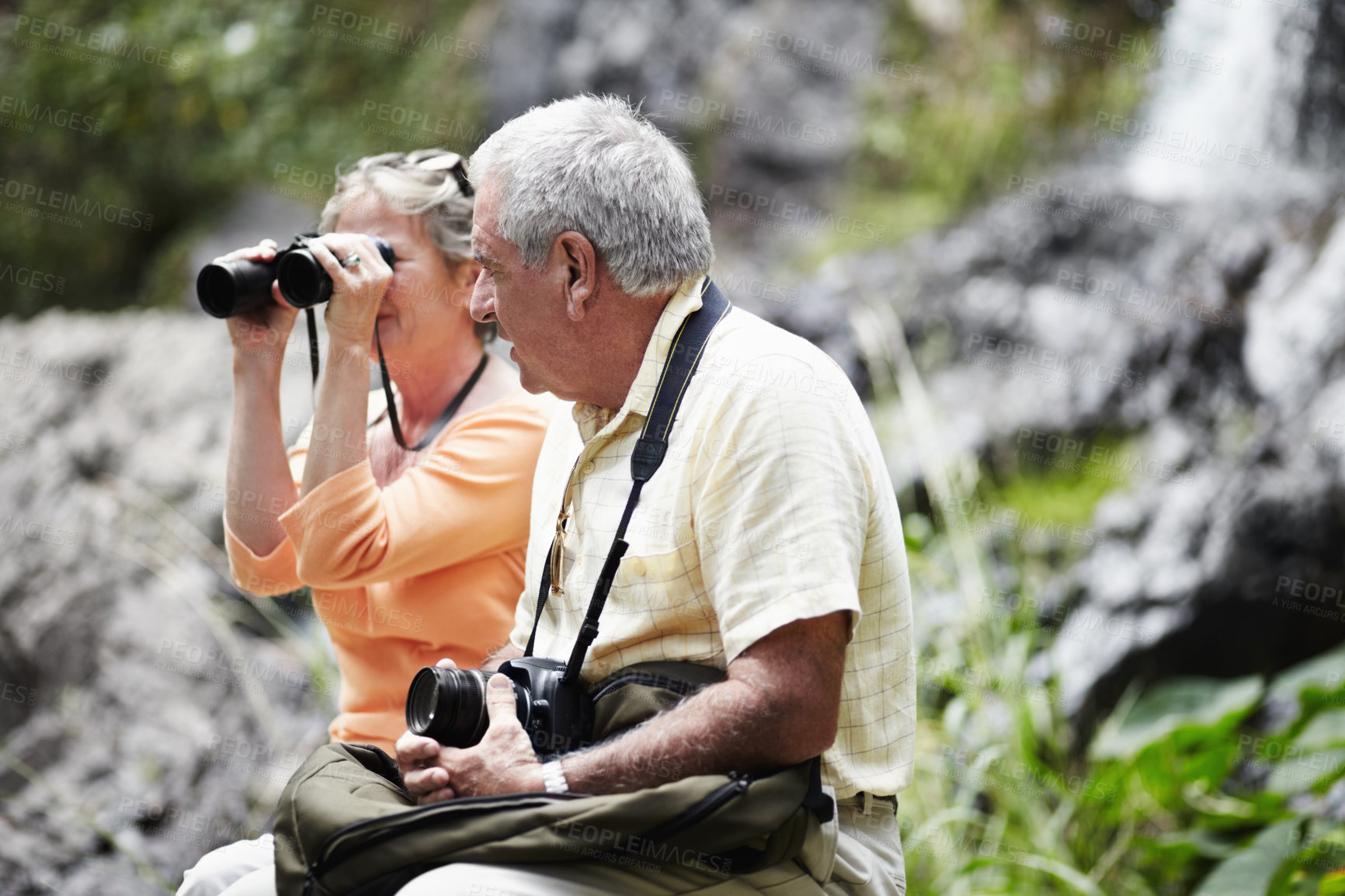 Buy stock photo Senior, couple and binocular in forest for tourist, sightseeing or vacation with waterfall and scenery. Elderly, man and woman in woods or nature for holiday, adventure or experience with backpack