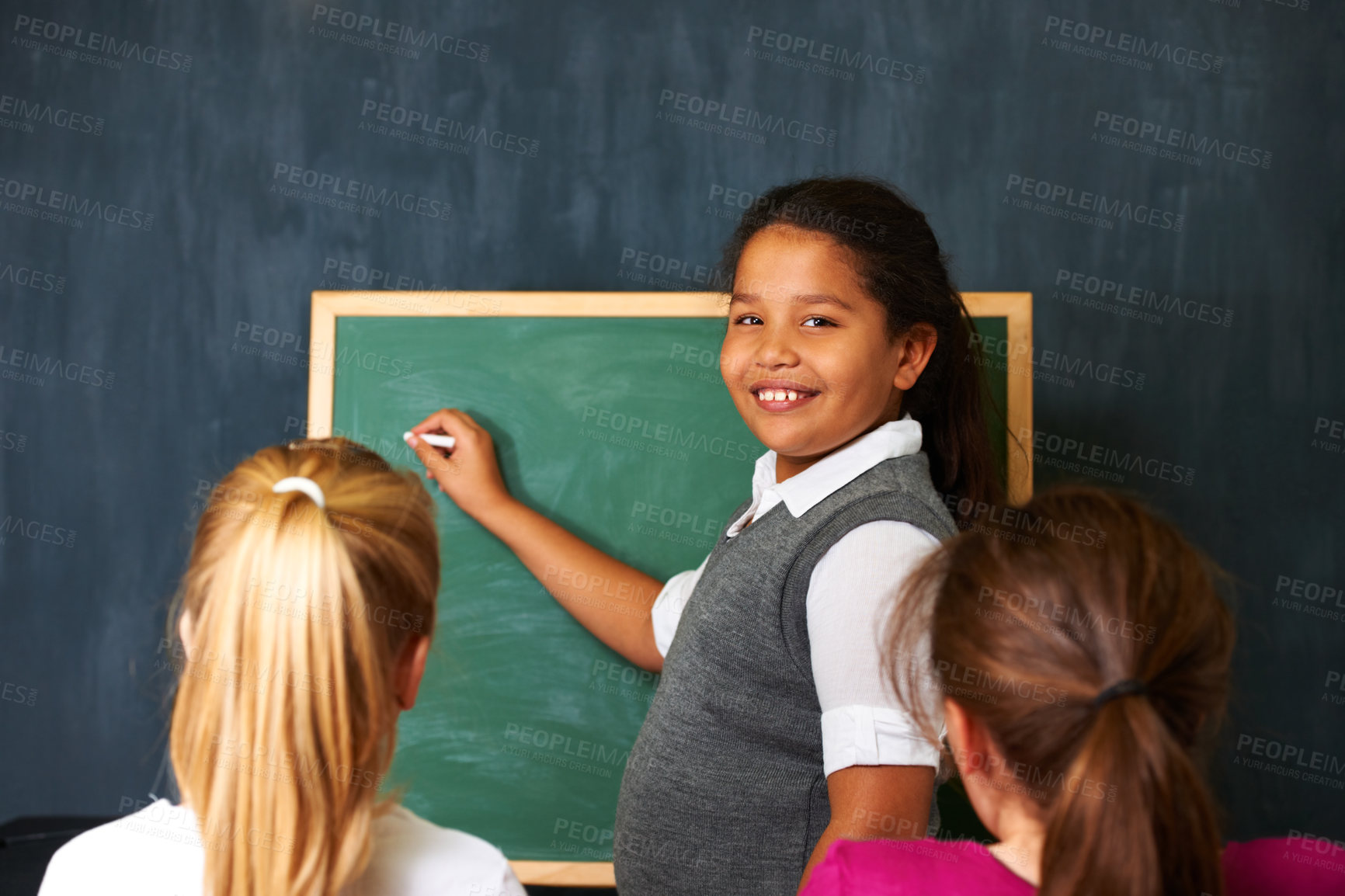 Buy stock photo Portrait of a cute girl showing her two friends something on the chalkboard in class