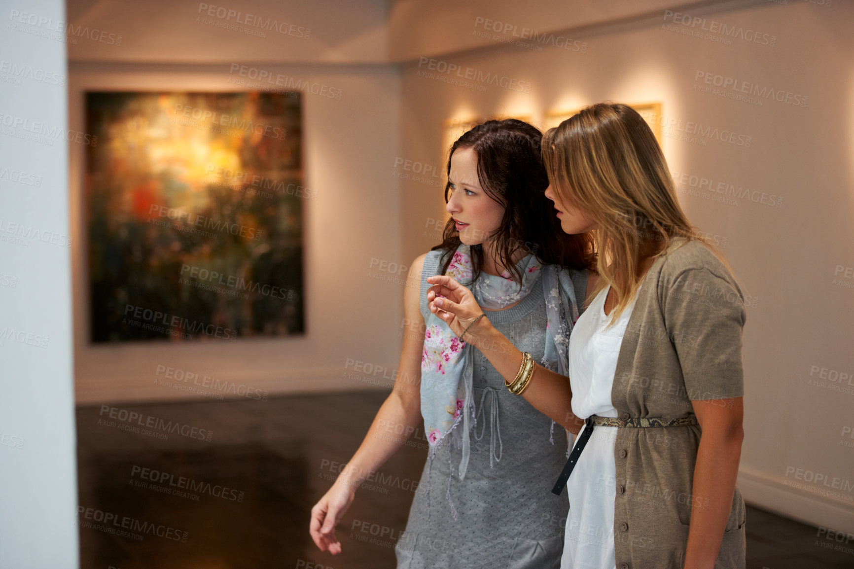 Buy stock photo Two young woman examining a painting up close while attending an exhibition