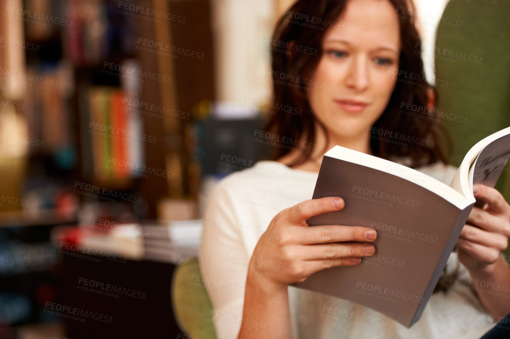Buy stock photo A young woman quietly reading a book while seated in a chair
